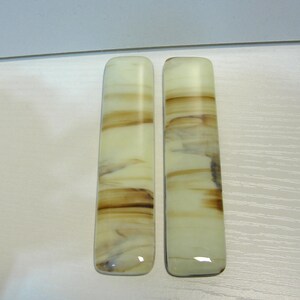 May include: Two rectangular, polished stone pieces with rounded edges. The stones have a creamy white base color with swirling bands of brown and tan, creating a marbled effect. The pieces are displayed side by side.