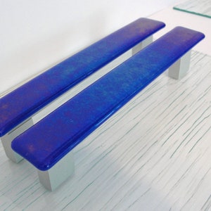 May include: Two blue glass cabinet door pulls with silver metal mounting plates.