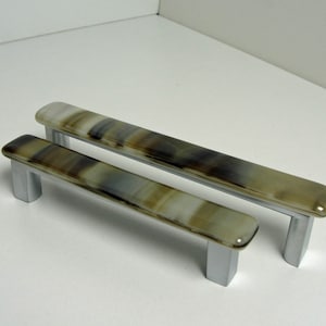 May include: Two glass cabinet pulls with a brown and white marbled pattern and silver metal bases.