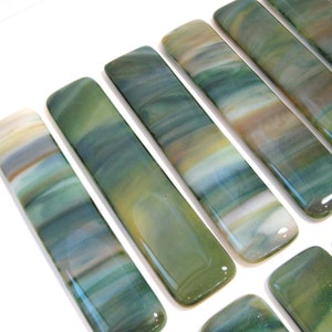 May include: A set of six glass tiles with a green, blue, and white marbled pattern. The tiles are rectangular and have a smooth, polished finish.