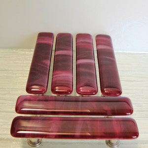 May include: Five glass cabinet knobs in a deep burgundy color with a swirling pattern. Two additional knobs are shown below, also in burgundy with a swirling pattern.