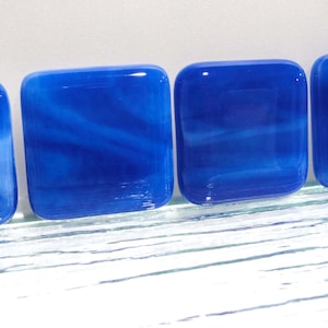 May include: Four blue glass coasters with a white swirl pattern. The coasters are square and have a glossy finish.