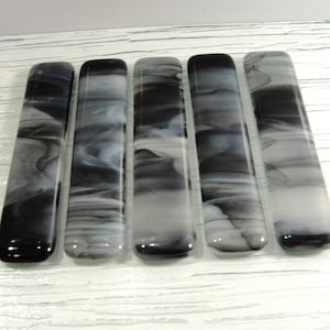 May include: Five black and white glass tiles with a marbled pattern. The tiles are rectangular and have rounded edges.