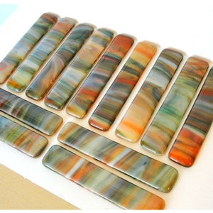 May include: A collection of colorful glass tiles with a swirled pattern in shades of orange, green, and blue. The tiles are rectangular and have a smooth, glossy finish.
