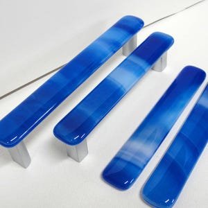 May include: Set of four blue and white glass cabinet pulls with brushed nickel hardware. The rectangular pulls have a rounded top and a gradient color pattern, transitioning from dark blue to white.