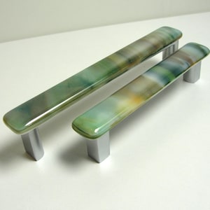 May include: Two glass cabinet door pulls with a green, white, and brown marbled pattern. The pulls have a silver metal base.