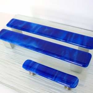 May include: Three blue glass cabinet pulls with a marbled effect. The pulls are different sizes and are arranged in a row from largest to smallest.
