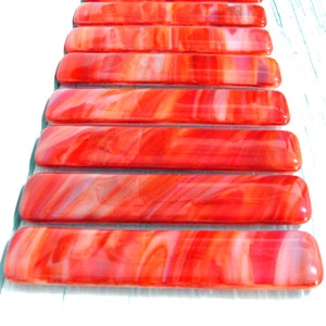 May include: A set of ten red and white glass tiles with a swirled pattern. The tiles are rectangular and have a glossy finish.