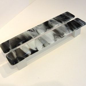 May include: Two black and white glass cabinet door pulls with a marbled design. The pulls are mounted on a silver base.