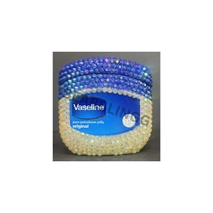 May include: A bedazzled jar of Vaseline petroleum jelly. The top is decorated with blue rhinestones, transitioning to a yellow base. The label reads "Vaseline pure petroleum jelly original".