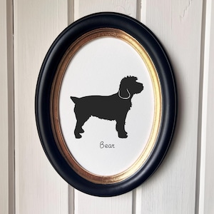 May include: An oval framed silhouette of a dog, with a black outline and a white background. The frame is black with a gold inner edge. The dog's name, "Bear", is written in a script font below the dog.