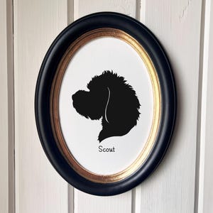 May include: An oval framed silhouette of a dog's head, in black against a white background. The frame is black with a gold inner edge. The dog's name, "Scout", is printed in black below the silhouette.