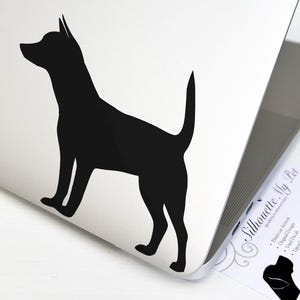 May include: Black silhouette of a dog on a white laptop. The dog is standing with its head turned to the left. The laptop is closed and the screen is facing the viewer. The image is a sticker for a laptop.