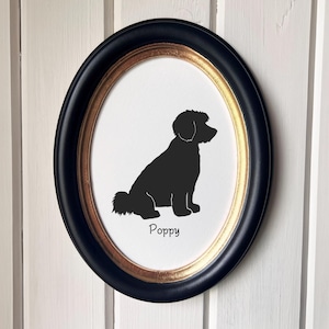 May include: Oval framed silhouette art of a dog, in black, with the name "Poppy" below the image. The frame is black with a gold inner border. The artwork is displayed against a white background.