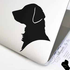 May include: A black silhouette of a dog's head and neck is displayed on a white laptop. The dog's profile is facing left, with a detailed outline. A business card with the text "Silhouette My Pet" is visible.