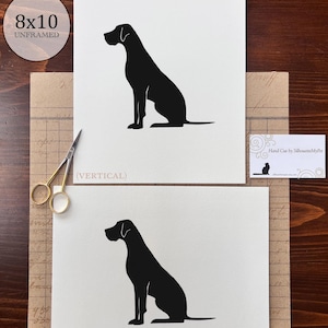 May include: Two prints of a black dog silhouette, one vertical and one horizontal, on white paper. The prints are labeled "8x10 UNFRAMED". The text "(VERTICAL)" and "(HORIZONTAL)" are below the prints. A business card reads "Hand Cut by SilhouetteMyPet".
