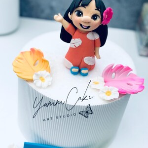 May include: A custom-made cake featuring a figurine of a cartoon character in an orange dress, with a pink flower in her hair. The cake is decorated with tropical leaves and flowers, and the name "Sofia 6" is displayed on a blue plaque.