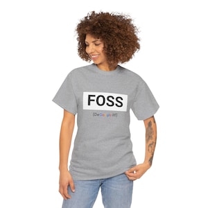 Op de afbeelding: Een lichtgrijs t-shirt met het woord "FOSS" in een witte rechthoek en de tekst "(DeGoogle it!)" eronder. Het shirt is een T-shirt met korte mouwen en een ronde hals.