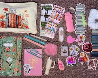 May include: An assortment of stationery and accessories, including a floral-printed notebook, a pink journal with a gold tree design, and a pencil case with a book and flower illustration. Also included are stickers, pens, and a fluffy scrunchie.