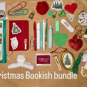 Könnte beinhalten: Eine Sammlung von weihnachtlichen Schreibwaren und Accessoires, darunter ein rotes Notizbuch, Aufkleber, Stifte und ein herzförmiger Schmuck. Der Satz "Christmas Bookish bundle" ist in weißer Schrift geschrieben.