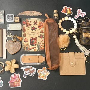 May include: An assortment of stationery and accessories, including a notebook with a bow design, pens, stickers, a pencil case, a bracelet, and a small purse. The items are arranged on a dark surface, with a Christmas theme.
