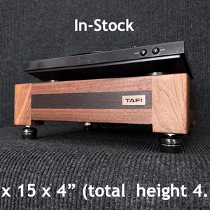 May include: A wooden turntable stand with a black top and a dark wood base. The stand is 18 x 15 x 4 inches (total height 4.5 inches) and features the text "TAFI". The text "In-Stock" is also visible.