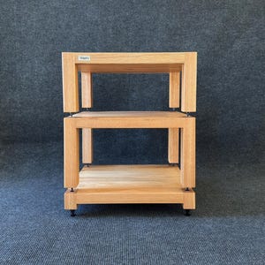 May include: A light brown, two-tiered wooden shelf unit with a rectangular design. The unit has a simple, modern aesthetic, with the brand name "TAFI" visible on the top shelf. The unit is designed to hold audio equipment or other items.