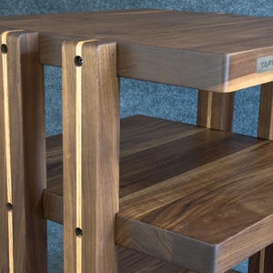 Puede incluir: Una mesa auxiliar de madera de dos niveles construida con madera de nogal marrón oscuro con acentos de grano de madera claro vertical en las patas. La mesa cuenta con una parte superior rectangular y un estante inferior, con una placa metálica TAFI.