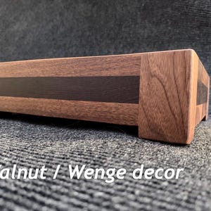 Peut inclure: Une boîte rectangulaire en bois avec un extérieur en noyer et un accent en bois de wengé foncé. La boîte est sur une surface grise. Le texte "Walnut / Wenge decor" est visible.