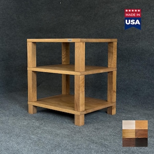 Puede incluir: Una estantería de madera de tres niveles con un acabado de veta de madera marrón claro natural. La estructura cuenta con cuatro postes esquineros verticales gruesos que sostienen tres estantes cuadrados. Una etiqueta metálica es visible.