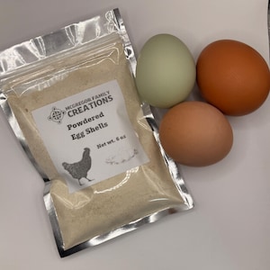 May include: A package of powdered egg shells from McGregor Family Creations, net weight 6 oz, next to three eggs in shades of green, orange, and brown. The package has a silver foil interior and a label with a hen illustration.