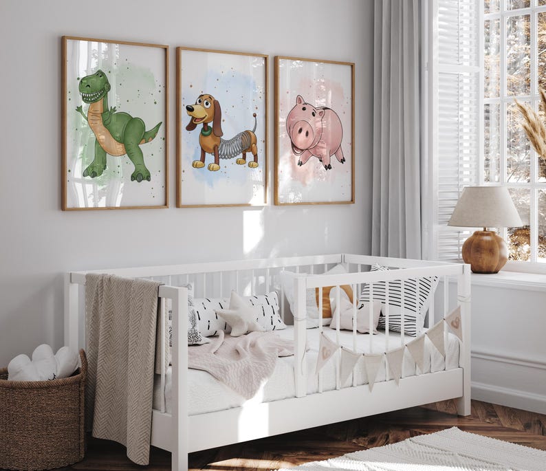 May include: Three framed art prints featuring cartoon characters: a green dinosaur, a brown dachshund with a spring body, and a pink pig. The prints are displayed above a white crib with a beige blanket and decorative pillows.