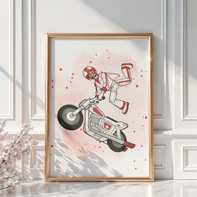 May include: A framed print featuring a cartoon illustration of a person in a white and red racing suit performing a stunt on a motorcycle. The motorcycle is white and red with black tires. The background is a light pink with red splatters.