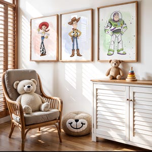 May include: Three framed prints of Toy Story characters, including Woody, Jessie, and Buzz Lightyear, hang on a white wall. A teddy bear sits on a white cabinet with a wooden top. A wicker chair with a teddy bear and a round ottoman are in the foreground.