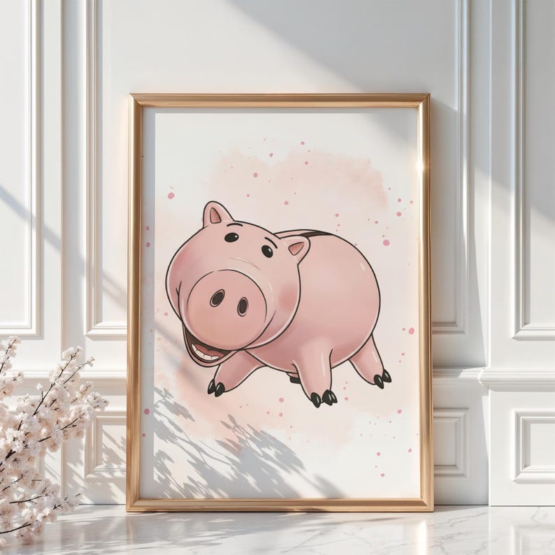 May include: A framed print featuring a cartoon pig character in shades of pink, with a smiling expression. The pig is set against a soft, watercolor-style background with pink speckles. The frame is gold.