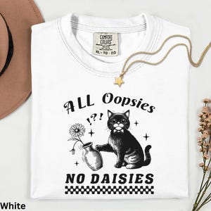 May include: White t-shirt with a black and white graphic of a cat, vase, and daisy, with the text "ALL Oopsies !?! NO DAISIES." The shirt has a crew neck and a tag that says "COMFORT COLORS XL-TG-EG."