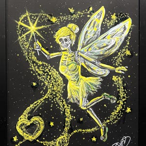 Puede incluir: Obra de arte enmarcada que representa un hada esquelética en amarillo y blanco sobre un fondo negro. El hada sostiene una varita en forma de estrella, con un rastro de chispas amarillas y una forma de corazón. La obra está firmada en la esquina inferior derecha.