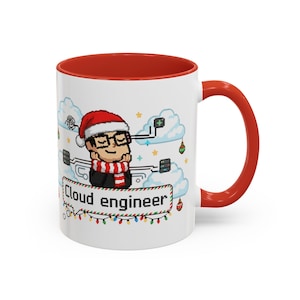 May include: White ceramic mug with a red interior and handle. The mug features a pixelated illustration of a person wearing a Santa hat and a scarf, with the words "Cloud engineer" on a banner. The design includes clouds, ornaments, and a string of lights.