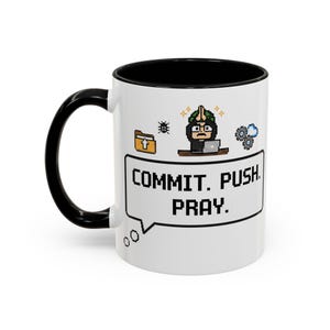 Könnte beinhalten: Weißer Keramikbecher mit schwarzem Innenraum und Henkel. Der Becher hat ein pixeliges Design mit dem Text "COMMIT. PUSH. PRAY." in einer Sprechblase sowie weitere pixelige Symbole.