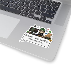 May include: A sticker showing a pixelated illustration of a person in a green beanie and glasses, at a computer. The speech bubble says, "Another day, another deployment..." The sticker is on a laptop.