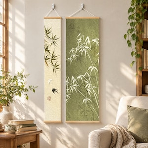 Peut inclure: Deux tentures murales verticales avec des motifs de bambou. La pièce de gauche est crème avec des feuilles de bambou vertes et deux petits oiseaux. La pièce de droite est vert olive avec des silhouettes de bambou blanches. Rails en bois.