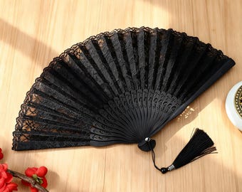 May include: A black hand fan with a lace design. The fan is open, displaying its intricate pattern and a tassel. The fan is made of wood and lace, and is a decorative accessory.