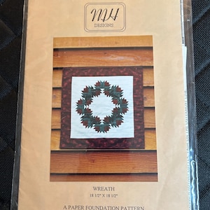 May include: A paper foundation pattern for a wreath quilt, featuring a square quilt design with a wreath of green and red leaves on a white background. The pattern is 18 1/2" x 18 1/2" and is from MH Designs.