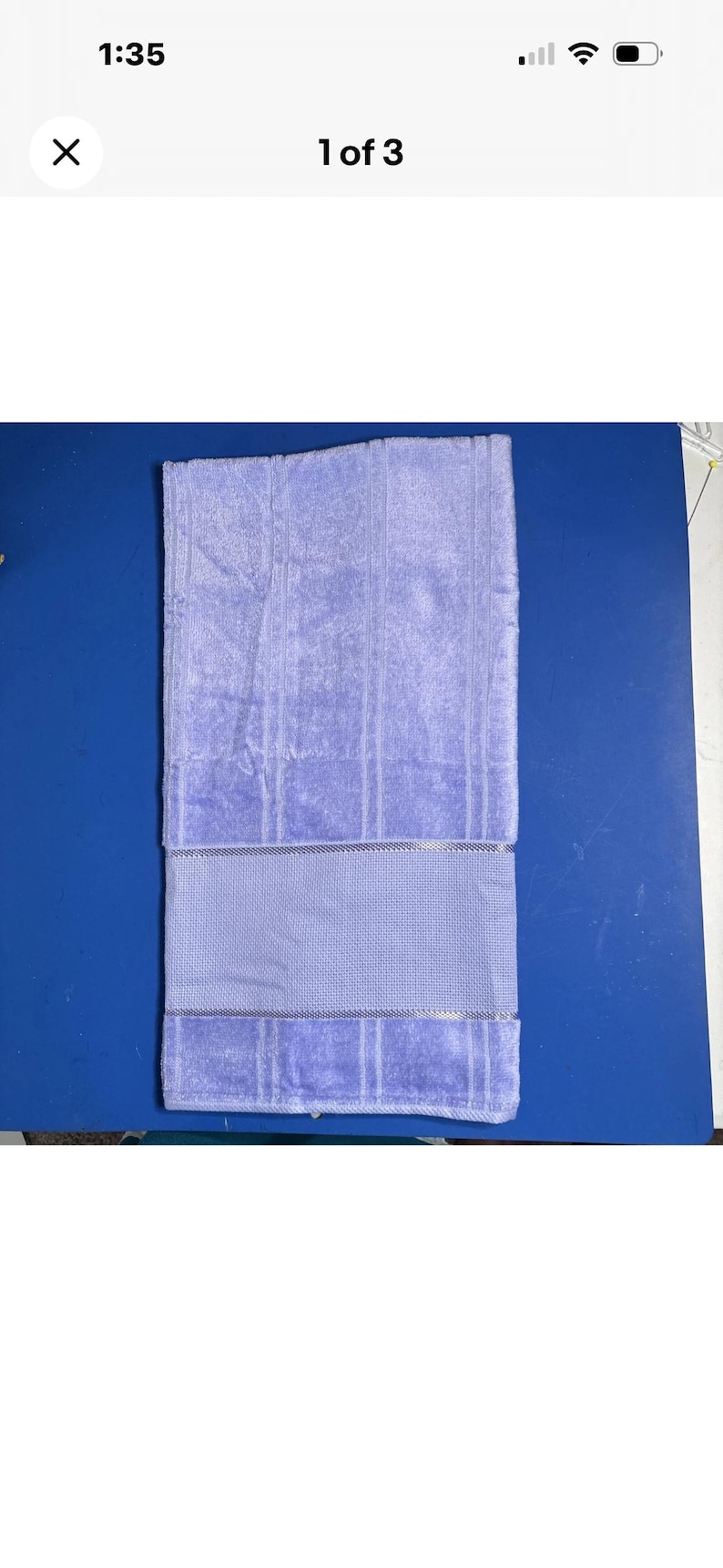 Pu&ograve; includere: Un asciugamano da bagno color lavanda con una superficie strutturata e una fascia decorativa. L'asciugamano &egrave; piegato e appoggiato su una superficie blu. L'asciugamano &egrave; di colore viola chiaro.
