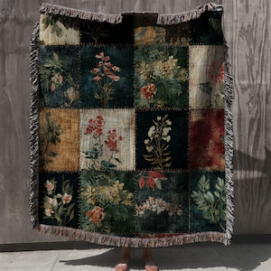 May include: A patchwork throw blanket featuring floral designs in various squares. The blanket has a dark green background with squares of different colors and floral patterns. The edges are fringed.