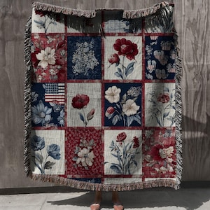 May include: A woven throw blanket with a patchwork design featuring floral patterns in red, white, and blue. The blanket has a fringed edge and includes an American flag motif, perfect for home decor.