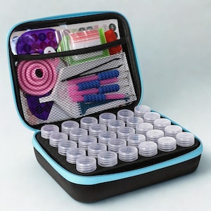 May include: Open black and blue zippered case with clear, round containers. The case contains various craft tools, including pink and blue tools, and a mesh pocket with additional supplies. The case is designed for organizing small craft items.