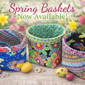 Könnte beinhalten: Drei bunte Stoffkörbe mit Blumen- und Mustermotiven, zusammen mit dekorierten Ostereiern. Die Körbe sind blau, grün und schwarz, mit dem Text "Spring Baskets Now Available!" im Hintergrund.