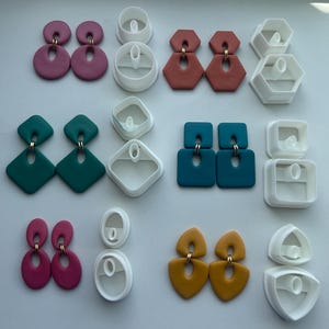 May include: A collection of six pairs of geometric polymer clay earrings in mauve, terracotta, teal, blue, magenta, and mustard, each paired with its corresponding white plastic clay cutter tool, arranged in a grid on a plain surface.
