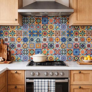 May include: A kitchen with light wood cabinets, a stainless steel range, and a colorful tile backsplash. The backsplash features a repeating pattern of square tiles with floral and geometric designs in various colors. A white pot sits on the stove.